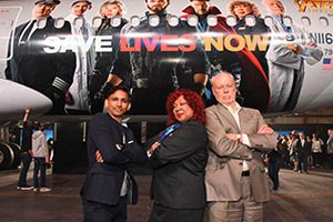 Dr. Phillip A. Sharp poses with, from left, Dr. Vinod Balachandran of Memorial Sloan Kettering Cancer Center in New York City and American Airlines staff member Shandra Fitzpatrick in front of an American Airlines jet at Los Angeles International Airport. The jet’s fuselage features Dr. Sharp and Dr. Balachandran, Marvel Comics superheroes, and American Airlines staff members. Photo by Araya Diaz/Getty Images for Stand Up To Cancer